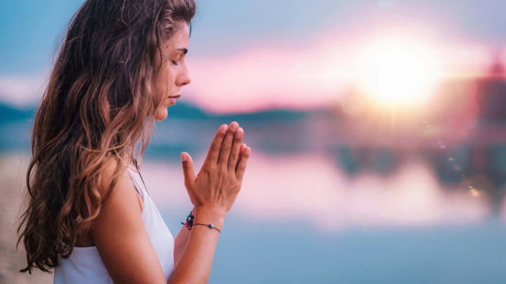 Woman meditating by a peaceful lake at sunset, practicing mindfulness and inner healing.